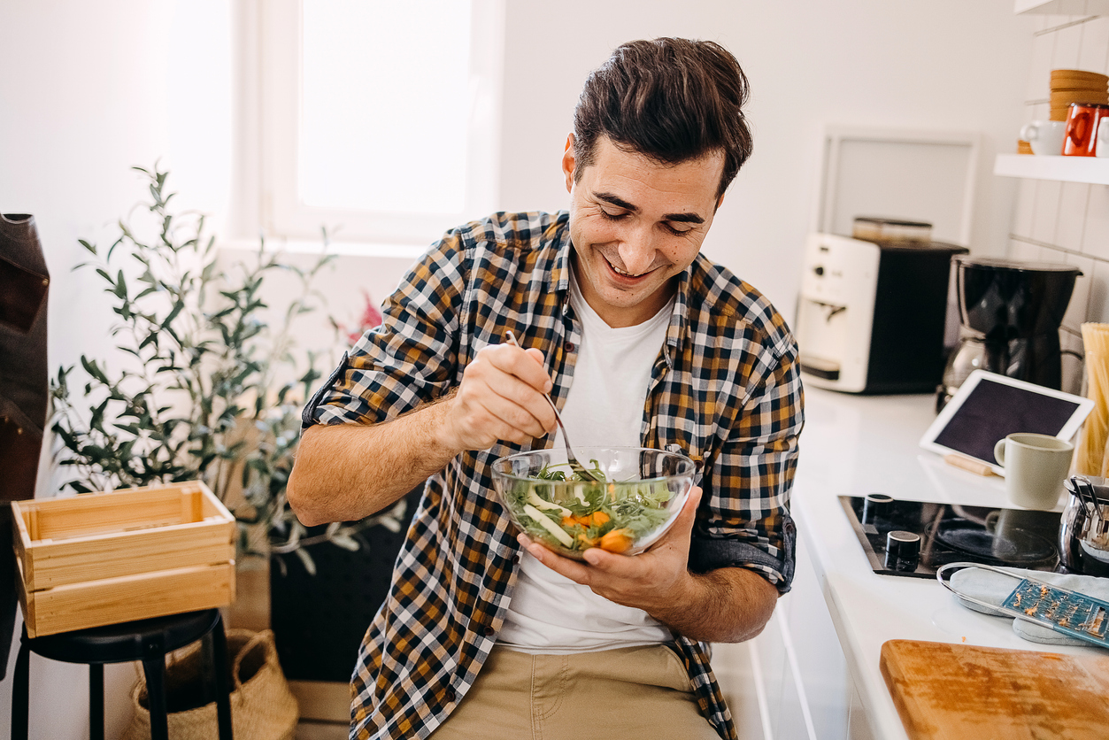 Young man eating a salad at home.