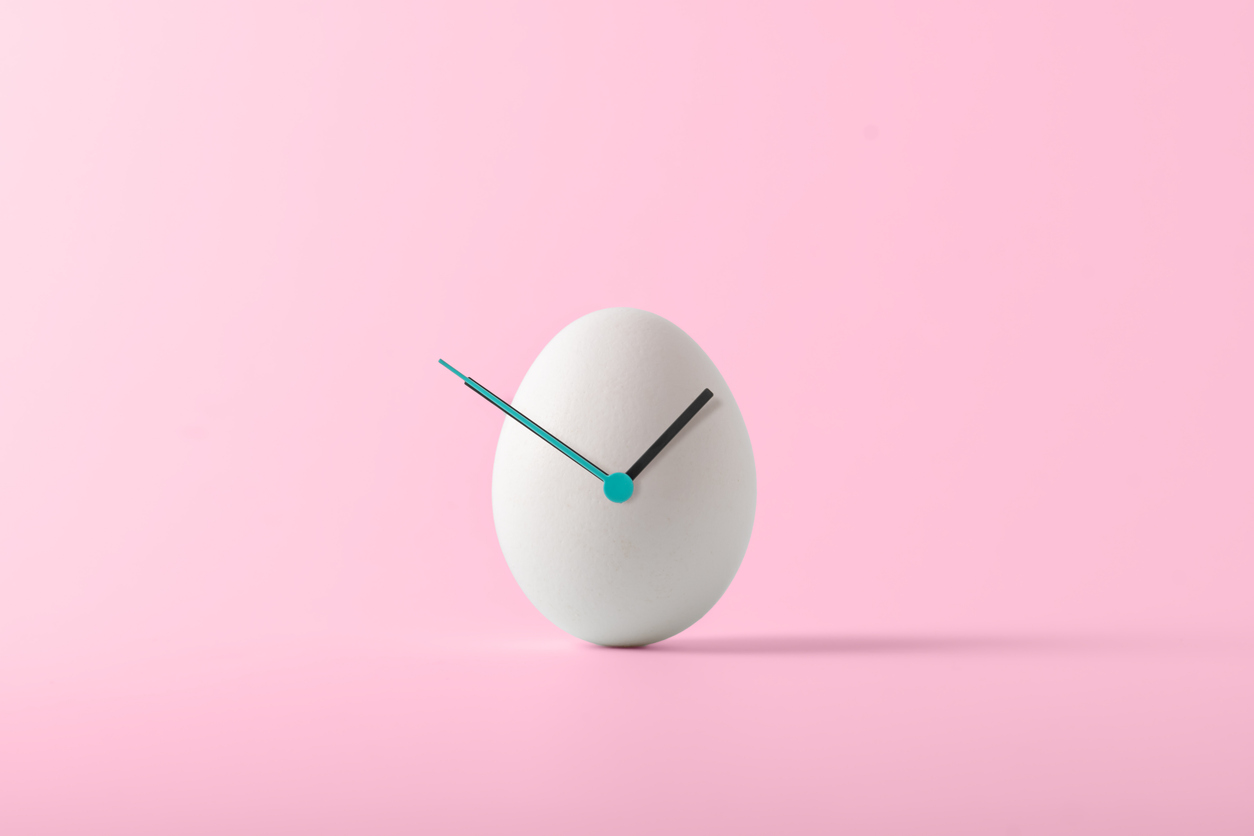 White Easter egg with hour hands on pink background.